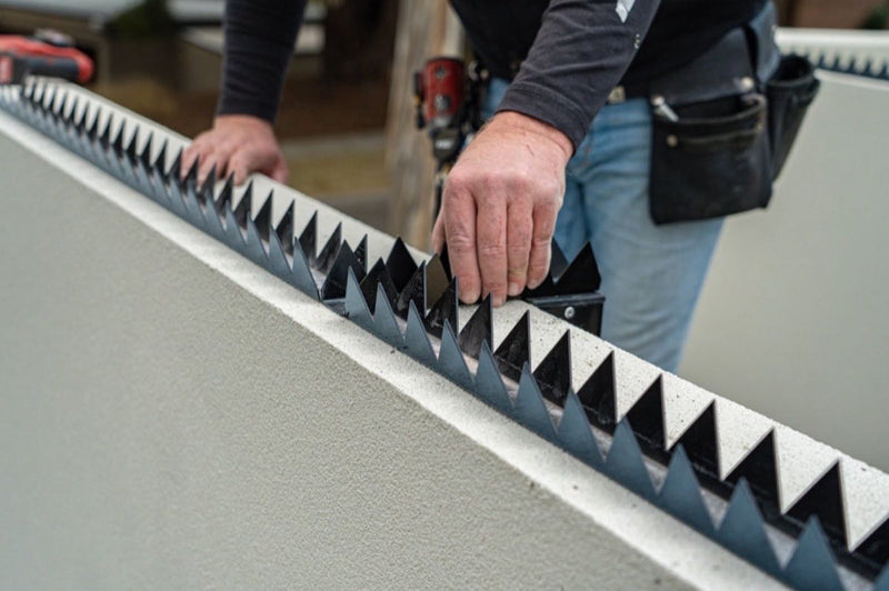 Installer fixing a croc top fence topper along the top of a wall